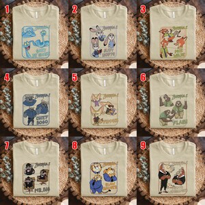 May include: Nine beige t-shirts with different Zootopia 2 character designs. Each shirt features a unique graphic, including characters like Gary, Judy Hopps, Nick Wilde, Chief Bogo, Finnick, Flash, Mr. Big, Clawhauser, and Yax.