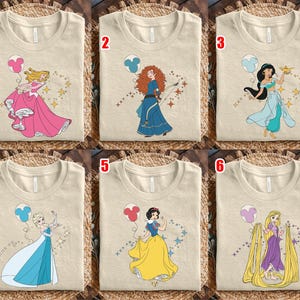 May include: Six beige t-shirts with different princess designs. Each shirt features a cartoon princess with a balloon and star accents. The princesses are in various poses and outfits, including pink, blue, and yellow dresses.