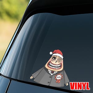 Op de afbeelding: Een vinyl sticker met een stripfiguur met een kerstmuts en een pak met een "Burgemeester" lint. Het personage heeft een brede grijns en spiraalogen. Het woord "VINYL" is rood.