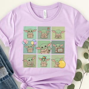 May include: A lilac t-shirt with a grid of nine cartoon illustrations of a green alien character. Each illustration shows the character in different poses, some holding balloons or a yellow ball. The shirt has a crew neck and short sleeves.