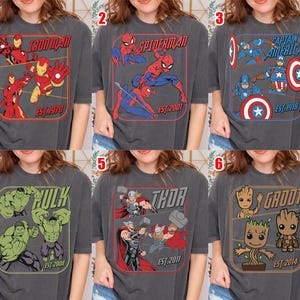 K&ouml;nnte beinhalten: Sechs graue T-Shirts mit Marvel-Comicfiguren. Jedes Shirt hat ein anderes Charakterdesign: Iron Man, Spider-Man, Captain America, Hulk, Thor und Groot. Jedes Design enth&auml;lt den Namen der Figur und das Jahr ihres Deb&uuml;ts.