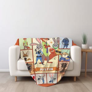 May include: A plush throw blanket featuring a colorful collage of characters from the animated movie Zootopia. The blanket has a cream-colored background with orange and brown accents. The name "JUSTIN" is displayed on a banner.