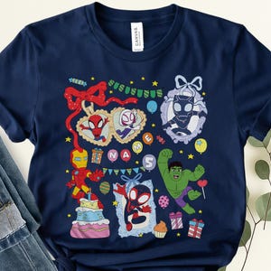 May include: A navy blue t-shirt featuring a colorful graphic print of various superheroes including Spider-Man, Iron Man, Hulk, and Black Panther. The design includes birthday-themed elements like a cake, gift boxes, balloons, and the text NAME 5.