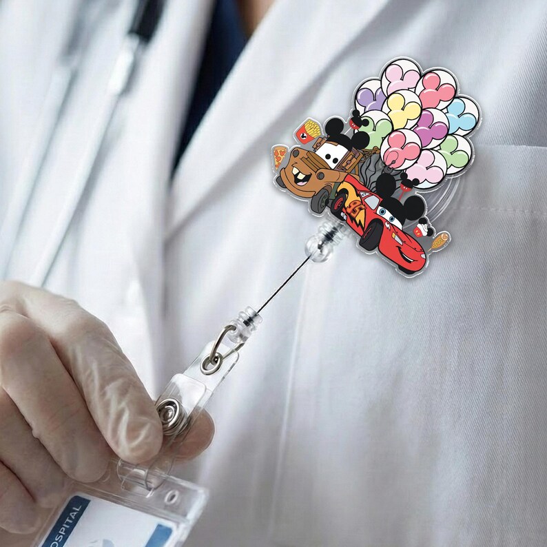 Op de afbeelding: Een intrekbare badge reel met stripfiguren Mater, Lightning McQueen en Mickey Mouse. De reel heeft een doorzichtige plastic behuizing en een zwart koord. De karakters zijn bevestigd aan een doorzichtige plastic schijf met kleurrijke hartvormige ballonnen.
