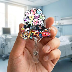 Op de afbeelding: Een kleurrijke badgehouder met cartoonauto's en Mickey Mouse-vormige ballonnen. De houder bevat afbeeldingen van Mater en Bliksem McQueen, met een doorzichtige plastic clip en een intrekbaar koord.