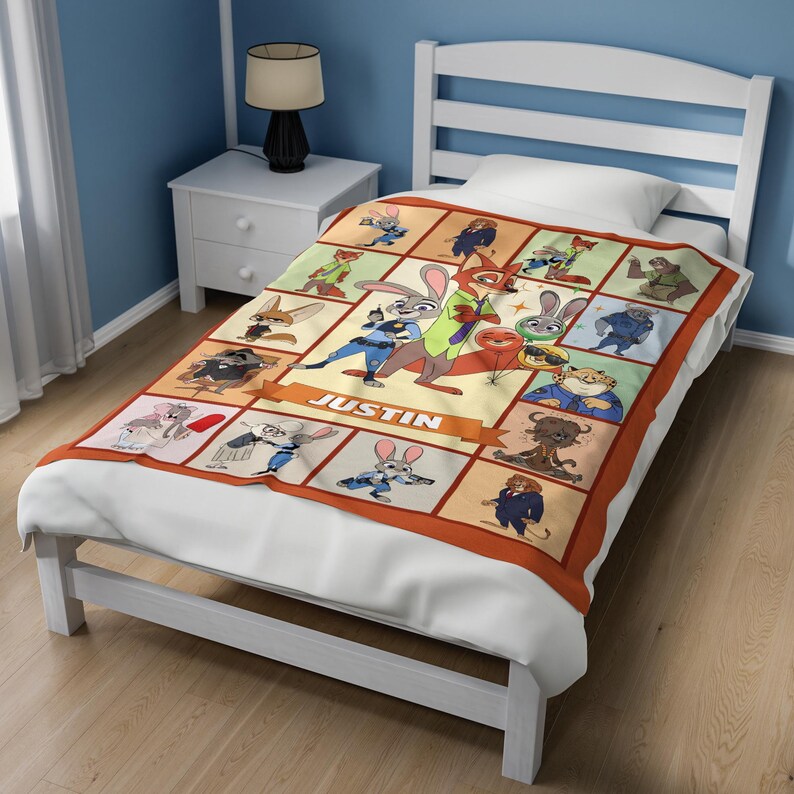 May include: A rectangular blanket featuring a grid of cartoon characters from the movie Zootopia. The blanket has a tan background with orange borders and the name "JUSTIN" in a banner. The blanket is placed on a white bed.