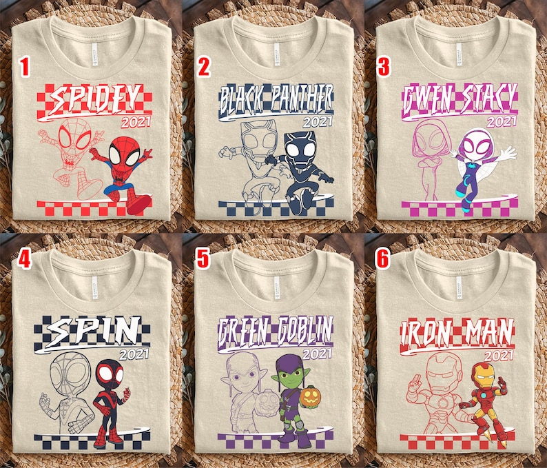 May include: Six beige t-shirts with superhero designs. Each shirt displays a different character's name and the year 2021. The designs include Spidey, Black Panther, Gwen Stacy, Spin, Green Goblin, and Iron Man.