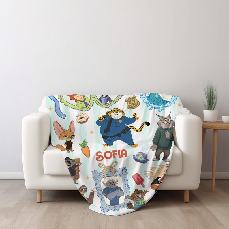 Puede incluir: Una manta blanca con personajes de dibujos animados y el nombre "SOFIA" en rojo. La manta tiene un fondo a rayas azul claro y blanco con varias ilustraciones de personajes, incluyendo un tigre con uniforme de polic&iacute;a y un zorro.