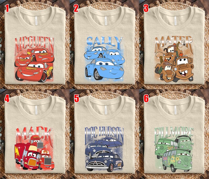 May include: Six beige t-shirts with different graphic designs featuring characters from the animated movie "Cars." The designs include "McQueen," "Sally," "Mater," "Mack," "Doc Hudson," and "Fillmore," each with corresponding car illustrations.