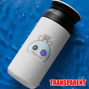May include: White insulated tumbler with a black lid and a cartoon character sticker. The sticker features a light blue head with a pink bow, a purple eye, and a stitched mouth. The word "TRANSPARENT" is printed in red.