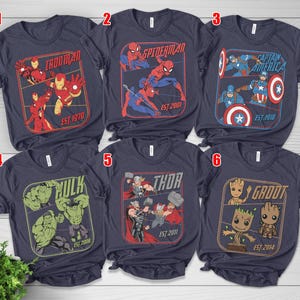 K&ouml;nnte beinhalten: Marineblaue T-Shirts mit Marvel-Charakteren: Iron Man, Spider-Man, Captain America, Hulk, Thor und Groot. Jedes Shirt zeigt eine Charaktergrafik in einem rechteckigen Rahmen, mit dem Namen und dem Gr&uuml;ndungsjahr des Charakters.