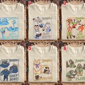 May include: Six beige t-shirts with different Zootopia 2 character designs. Each shirt features a rectangular graphic with characters like Gary De Snake, Judy Hopps, Nick Wilde, Chief Bogo, Finnick, and Flash.