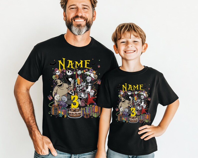 Pode incluir: T-shirts pretas com um gr&aacute;fico colorido com personagens de "O Estranho Mundo de Jack" e o n&uacute;mero "3". As camisas t&ecirc;m a palavra "Name" acima do gr&aacute;fico e s&atilde;o usadas por um homem e uma crian&ccedil;a.