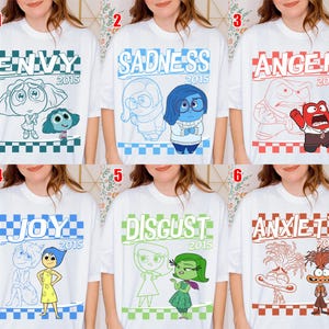May include: White t-shirts with various Inside Out character designs. Each shirt features a different emotion: Envy, Sadness, Anger, Joy, Disgust, and Anxiety, along with the year 2015. The designs are outlined in different colors.