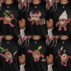Puede incluir: Camisetas negras con personajes de dibujos animados. Los personajes tienen cabezas de coco y extremidades rosas. Cada dise&ntilde;o presenta un personaje &uacute;nico con accesorios como lanzas, garrotes y tocados. Las ilustraciones son coloridas y caprichosas.