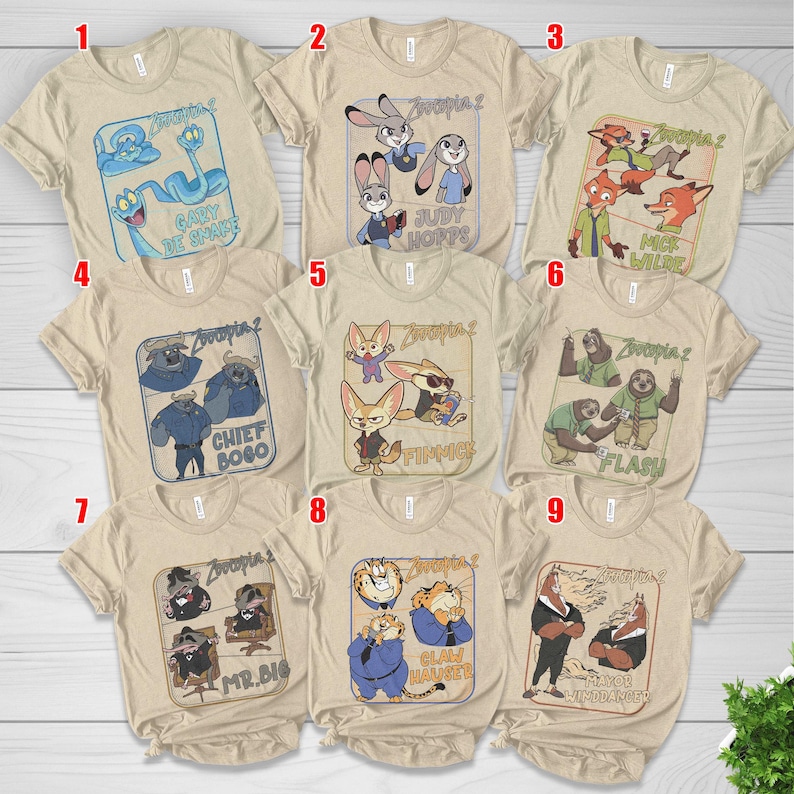 May include: A collection of nine beige t-shirts featuring characters from the animated film "Zootopia 2". Each shirt displays a different character or group of characters with their names. The shirts have short sleeves and a crew neck.