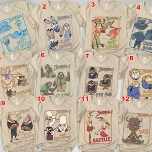 May include: A collection of beige t-shirts featuring various characters from the animated film "Zootopia 2". Each shirt displays a different character or group of characters with their names, such as "Judy Hopps" and "Nick Wilde".