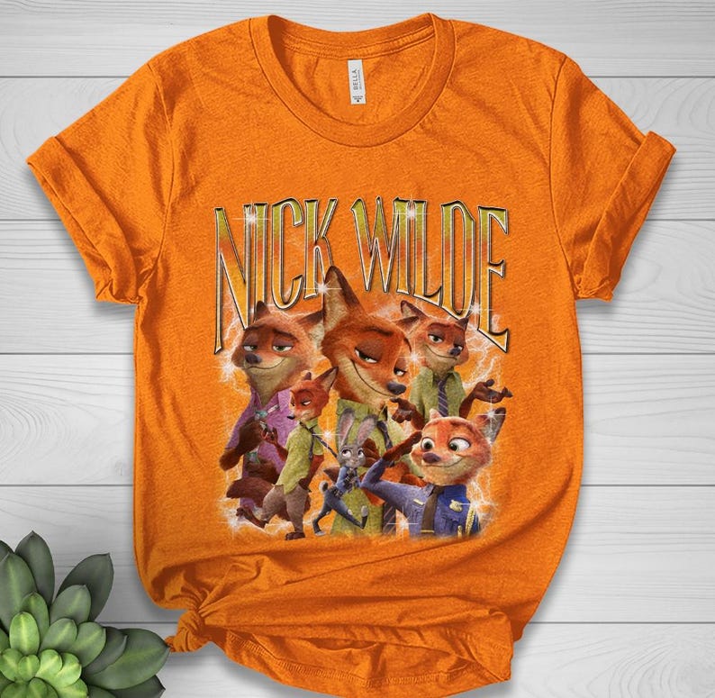May include: Orange t-shirt featuring a graphic of Nick Wilde from Zootopia. The design includes multiple images of the character with the text "NICK WILDE" in gold lettering. The shirt is made of a soft material.