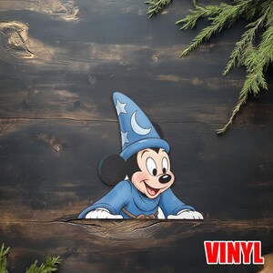 Puede incluir: Un recorte de vinilo de Mickey Mouse con un disfraz de mago azul con un sombrero decorado con una luna creciente y estrellas. El recorte est&aacute; sobre una superficie de madera oscura con la palabra "VINYL" en rojo.