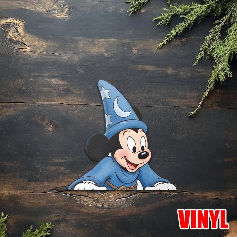 Puede incluir: Un recorte de vinilo de Mickey Mouse con un disfraz de mago azul con un sombrero decorado con una luna creciente y estrellas. El recorte est&aacute; sobre una superficie de madera oscura con la palabra "VINYL" en rojo.