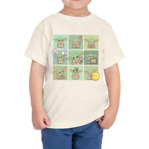 May include: A cream-coloured toddler t-shirt with a grid of nine cartoon images of a green alien character. Each image shows the character in different poses, some holding objects like balloons and a ball.