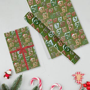 May include: Green wrapping paper with a repeating pattern of the numbers 67, some with Santa hats. A wrapped gift with a red ribbon and a roll of the same paper are displayed. Festive holiday theme.