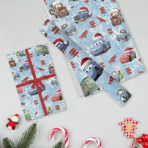 May include: Light blue wrapping paper featuring cartoon cars wearing Santa hats and snowflakes. A wrapped gift with a red ribbon and bow is next to a roll of the same paper. Christmas-themed gift wrap.