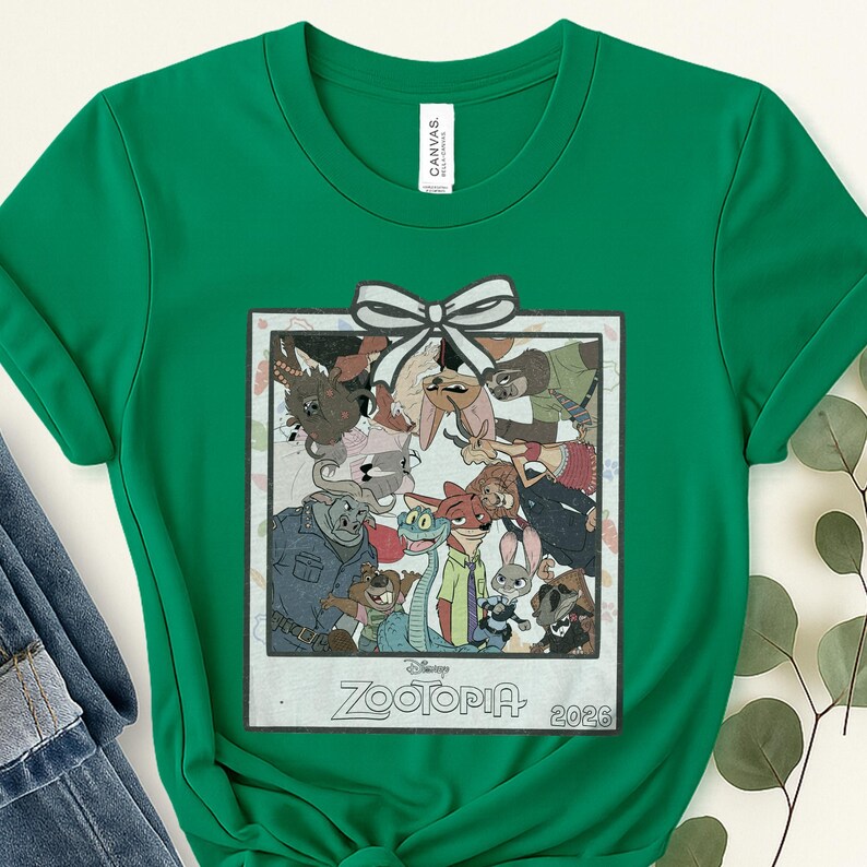 Puede incluir: Una camiseta verde con un gr&aacute;fico enmarcado de personajes de la pel&iacute;cula de Disney Zootopia. El gr&aacute;fico incluye un lazo blanco y el texto "Zootopia 2026". La camiseta est&aacute; hecha de un material suave y es adecuada para uso casual.
