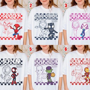 May include: White t-shirts featuring superhero designs. The shirts display graphics of "Spidey," "Black Panther," "Gwen Stacy," "Spin," "Green Goblin," and "Iron Man," each with "2021" text. The illustrations are in red, black, and blue.