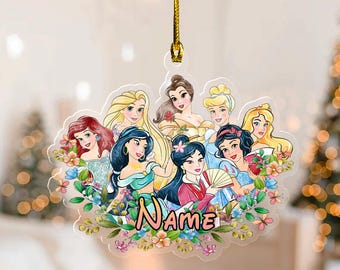 May include: A clear, snowflake-shaped ornament featuring illustrations of several princesses surrounded by colorful flowers. The word "Name" is written in a playful font across the bottom. A gold string is attached for hanging.