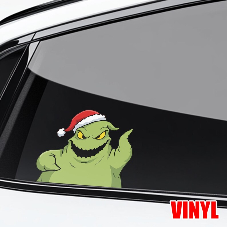 Op de afbeelding: Een groen stripfiguur met een kerstmuts, een sinistere grijns en gele ogen, staat op een autoruit. Het woord "VINYL" staat rechtsonder in het rood gedrukt. De sticker is ontworpen voor autodecoratie.