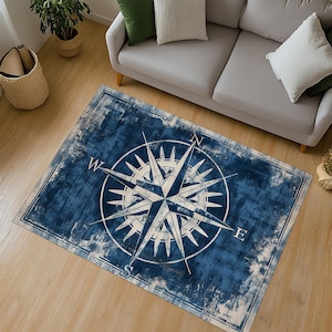 Könnte beinhalten: Ein blauer und weißer Teppich mit einem abgenutzten Look zeigt ein Kompassdesign mit den Buchstaben N, S, E und W. Der Kompass ist von einem Kreis aus Sternen umgeben.