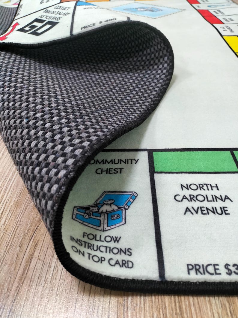 May include: A close-up of a Monopoly board game rug with a black and gray checkered backing. The rug features the Community Chest and North Carolina Avenue spaces. The text "Follow instructions on top card" is visible.
