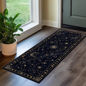 Könnte beinhalten: Ein rechteckiger Läufer mit dunkelblauem Hintergrund und goldenem Himmelsmuster. Das Design zeigt verschiedene Sterne, Sternbilder und Mondphasen, die über die Oberfläche und entlang der dekorativen Ränder verteilt sind.