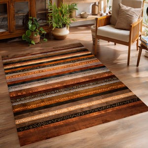 May include: A rectangular area rug with a striped pattern in shades of brown, black, and white. The rug features various textures and designs within each stripe, creating a rustic and textured appearance. The rug is placed on a wooden floor.