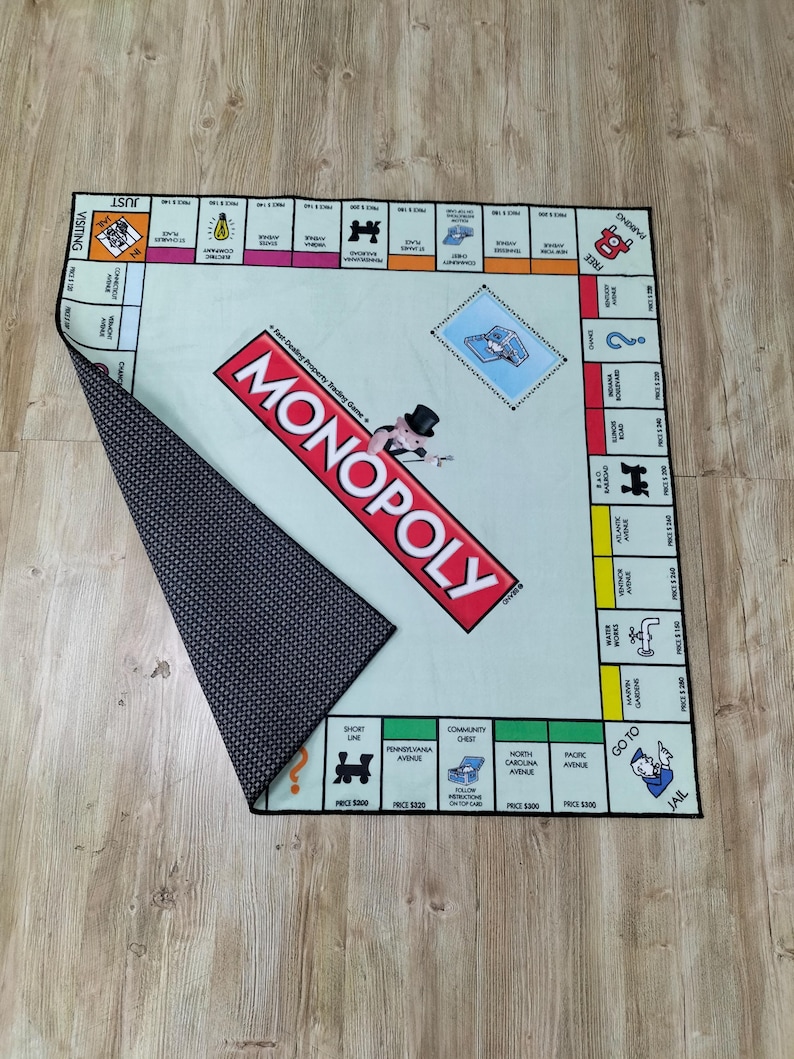 May include: A Monopoly board game mat with a light green playing surface and a black and white patterned underside. The Monopoly logo is prominently displayed in red. The board game's properties and spaces are visible.