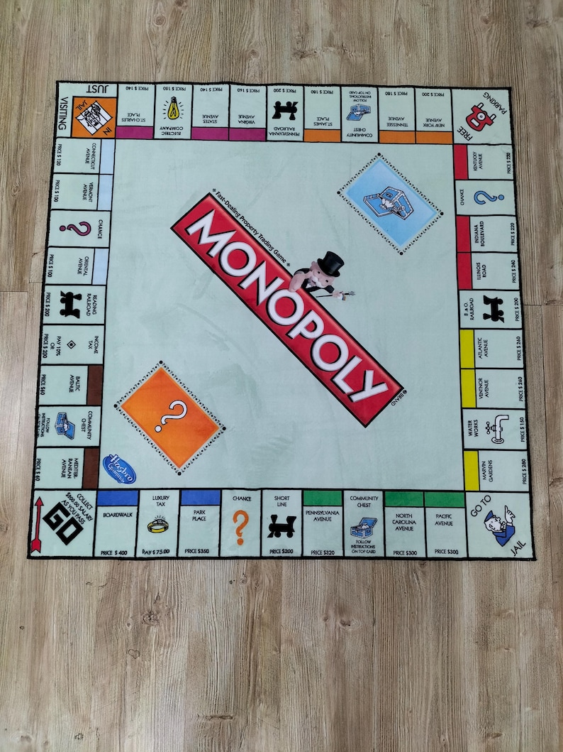 May include: A Monopoly board game rug with a light blue center and a red Monopoly logo. The game board features property spaces, Chance and Community Chest cards, and the Go to Jail space. The rug is designed for playing the classic board game.