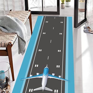 Könnte beinhalten: Rechteckiger Teppich mit einem Landebahndesign in Blau und Grau. Ein weißes und blaues Flugzeug befindet sich am Ende der Landebahn. Der Teppich hat einen blauen Rand.