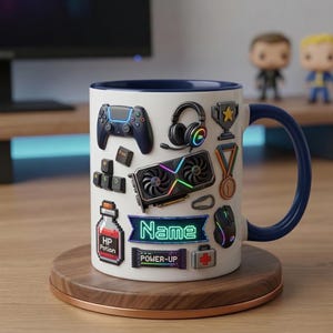 May include: White ceramic mug with a blue handle and rim, decorated with gaming-themed graphics. Includes a controller, headphones, keyboard keys, a graphics card, and the word "Name" in a neon sign style. The mug sits on a wooden coaster.