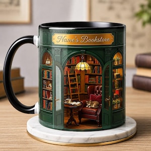 Può includere: Una tazza in ceramica con manico nero caratterizzata da un design a vetrina verde con il testo Name's Bookstore. L'illustrazione raffigura l'interno di un'accogliente biblioteca con scaffali, una scala, una poltrona in pelle, un gatto e lampada.