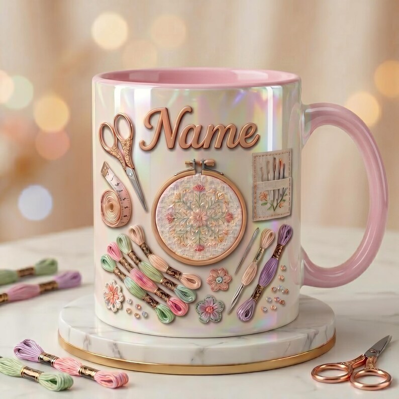 May include: A pearlescent ceramic mug with a pink interior and handle, featuring a printed design of embroidery supplies including scissors, a measuring tape, an embroidery hoop, needles, and colorful thread skeins with the word Name.