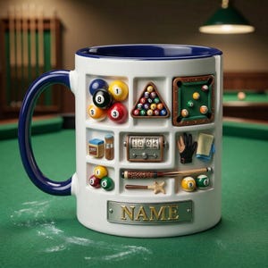 May include: White ceramic mug with a blue handle and rim, decorated with various 3D elements related to billiards. Features pool balls, a triangle rack, a table, and a nameplate. The mug is set against a green felt surface.
