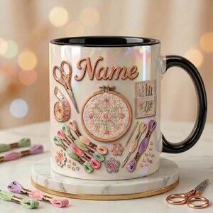 May include: A white iridescent ceramic mug with a black interior and handle, featuring the word Name in script font, an embroidery hoop, scissors, needles, and colorful embroidery floss skeins printed on the exterior surface of the mug.