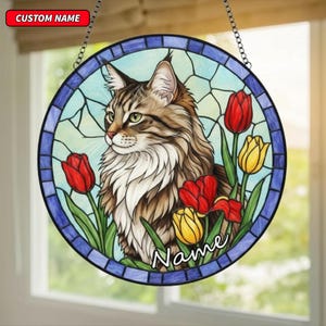 Könnte beinhalten: Rundes Buntglasfenster mit einer Katze mit braun-weißem Fell, grünen Augen und roten und gelben Tulpen. Die Wörter "CUSTOM NAME" und "Name" sind sichtbar. Das Kunstwerk hat einen blauen Rand und eine Kette zum Aufhängen.