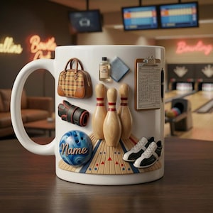 Könnte beinhalten: Weiße Keramiktasse mit Bowling-Elementen verziert. Mit einem Bowlingball mit dem Namen "Name", Bowlingkegeln, Schuhen, einer Bowlingtasche und einem Spielzettel. Die Tasse hat einen großen Henkel und steht vor einem verschwommenen Bowlingbahn-Hintergrund.