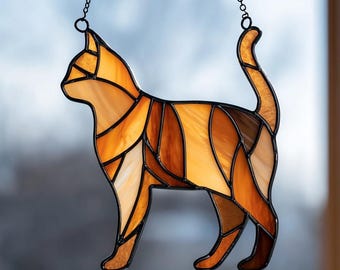 May include: Stained glass cat silhouette in shades of orange, brown, and cream, with a black metal outline and chain for hanging. The cat is depicted in a standing pose, with its tail curved upwards. A decorative item for cat lovers.