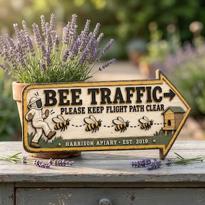 Peut inclure: Un panneau en bois en forme de flèche avec un fond crème et une bordure jaune. Il porte le texte BEE TRAFFIC, PLEASE KEEP FLIGHT PATH CLEAR et HARRISON APIARY EST. 2019. Les graphismes incluent un apiculteur, quatre abeilles et une ruche.
