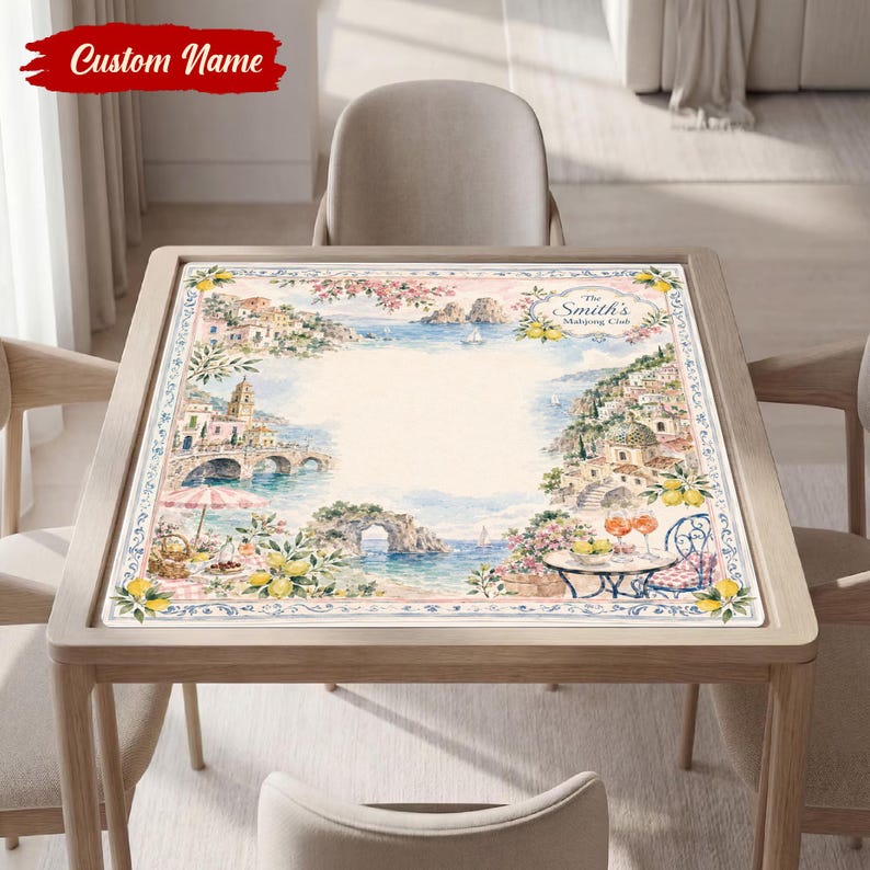 May include: A square table mat featuring a watercolor coastal scene with Mediterranean-style buildings, lemon branches, and a seaside terrace. The text "The Smith's Mahjong Club" is printed in the upper right corner of the illustrated border.