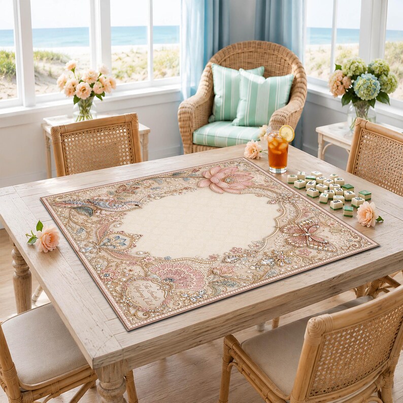 May include: A square game board featuring a cream-colored center surrounded by an ornate border of pink lotus flowers, butterflies, and intricate gold-toned filigree patterns. The board is placed on a wooden table with scattered game tiles.