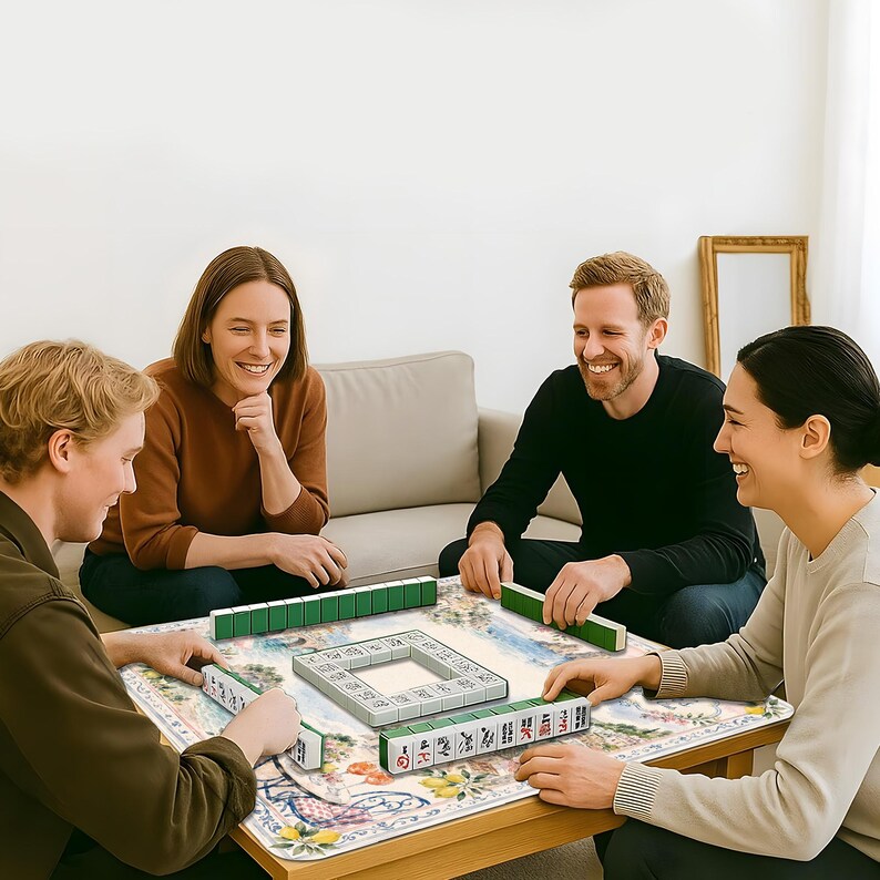May include: A mahjong game set featuring white tiles with green backs and black, red, and green character markings. The tiles are arranged in a square formation on a rectangular mat with a colorful floral and fruit pattern on a wooden table.